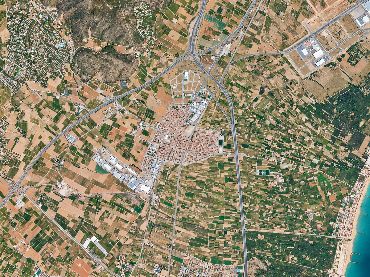 Vista aérea de un núcleo urbano, parcelas agrícolas, áreas residenciales, carreteras y costa