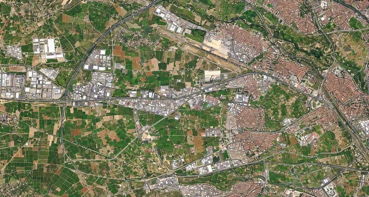 Vista aérea de núcleos urbanos, áreas industriales, campos, carreteras y una pista de aeropuerto
